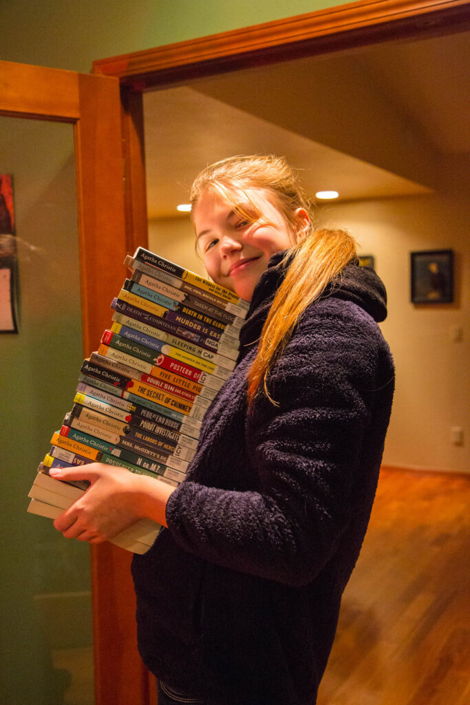 My daughter holds a stack of Agatha Christie mysteries. Place a paper book by your pillow to remind yourself of your intention..